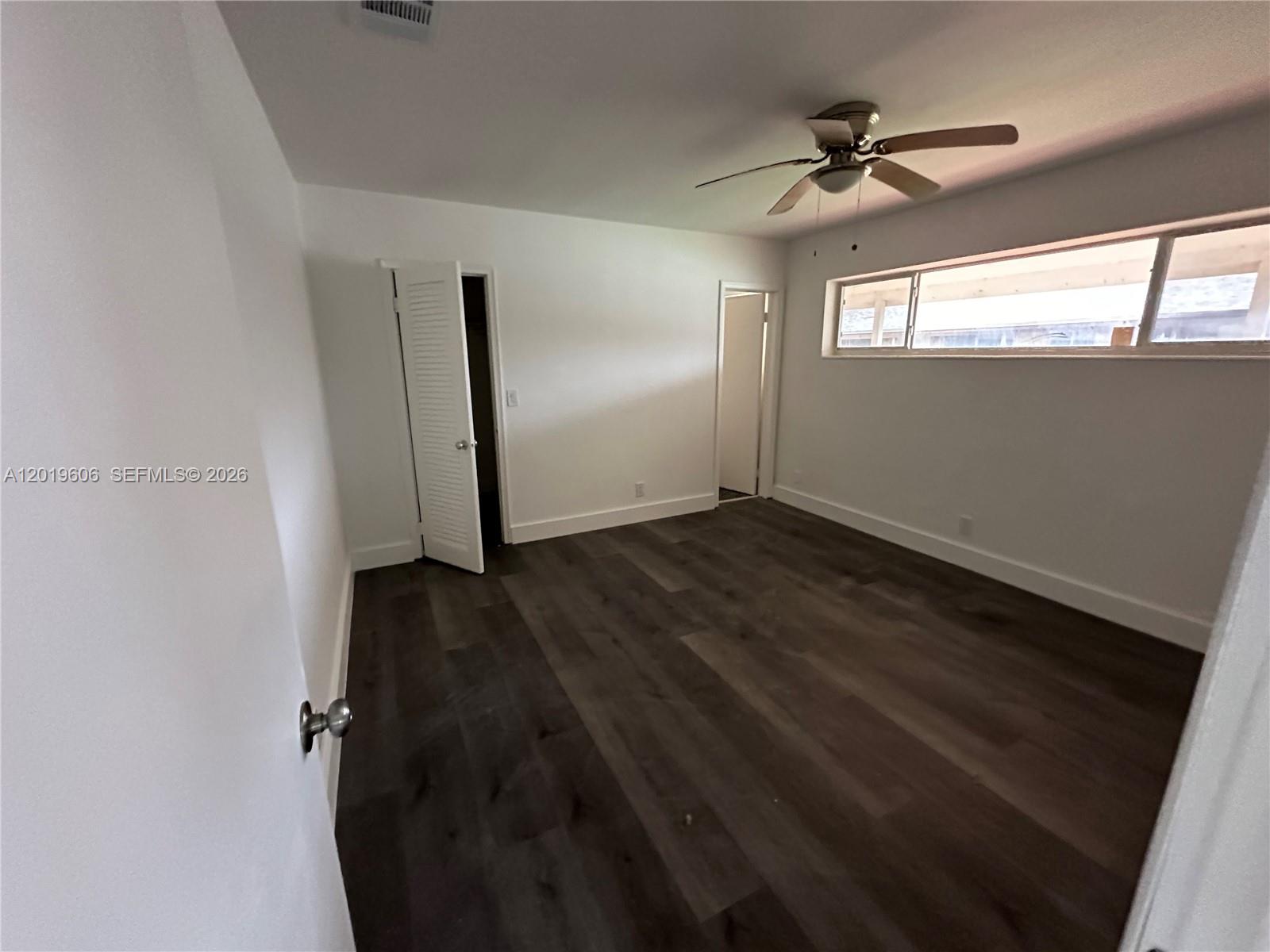 An empty bedroom features white walls, dark wood-look flooring, a ceiling fan, and two doorways — 117 SE 2nd Ave # 1, Hallandale Beach FL 33009, HALLANDALE BEACH, FL