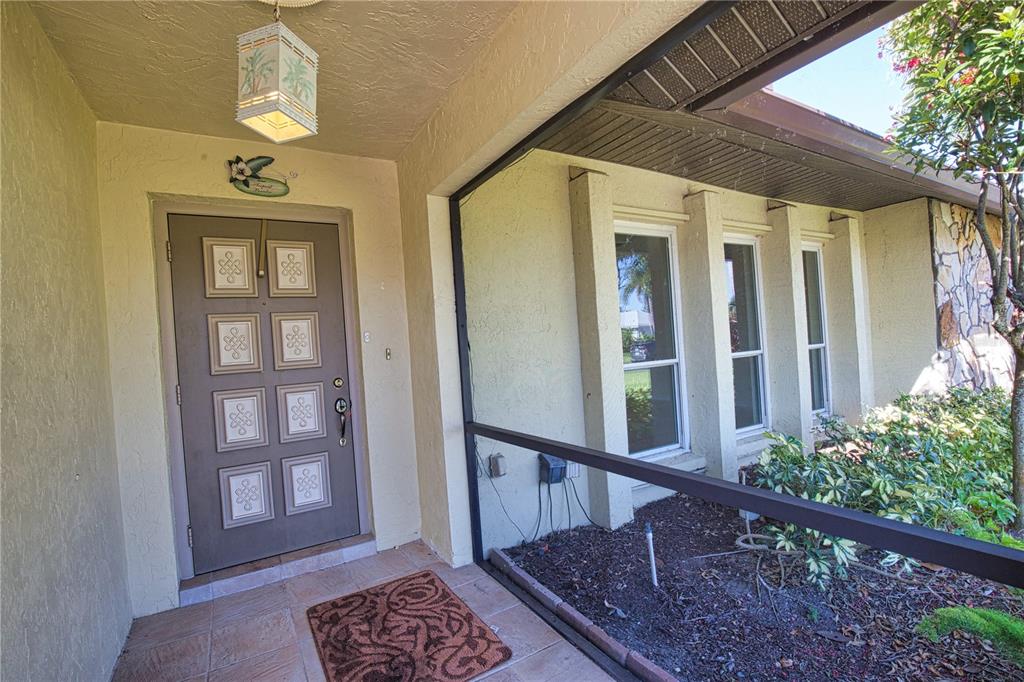 A covered entryway features a brown front door with decorative panels and tiled flooring — 902 PINEHURST LANE, VENICE, FL