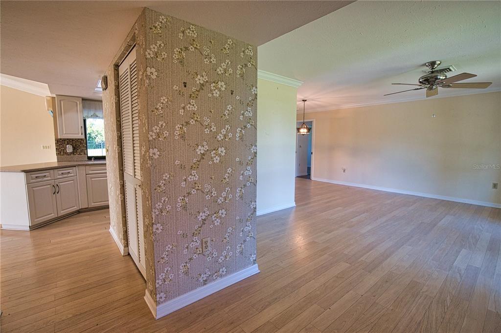 A kitchen with white cabinets and a floral wallpapered wall opens to a living area — 902 PINEHURST LANE, VENICE, FL