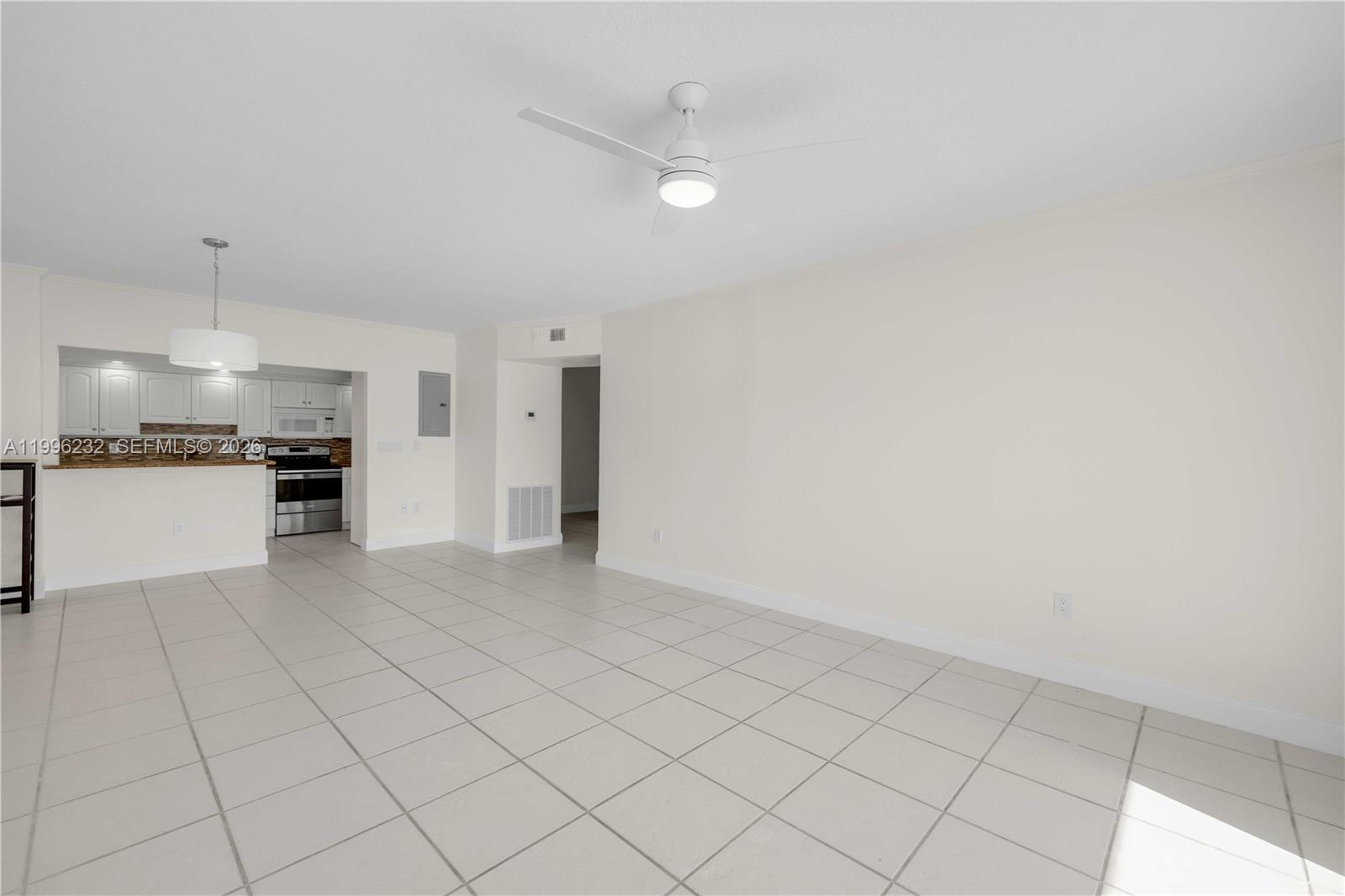An open-concept living area features white tile flooring, a ceiling fan, and an adjacent kitchen — 462 Golden Isles Dr # 210, Hallandale Beach FL 33009, HALLANDALE BEACH, FL
