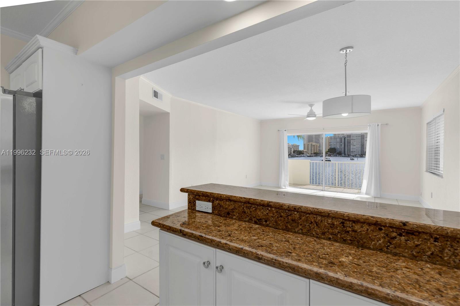 A kitchen breakfast bar with granite countertops overlooks a living area with a balcony view — 462 Golden Isles Dr # 210, Hallandale Beach FL 33009, HALLANDALE BEACH, FL
