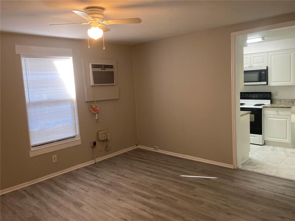 A room with gray wood-look flooring, a ceiling fan, a window unit, and a kitchen view — 2004 2ND AVE UNIT 2, BRADENTON, FL