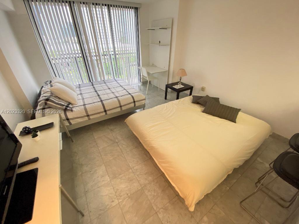 A bedroom features two beds, tile flooring, a desk, and floor-to-ceiling vertical blinds — 540 Brickell Key Dr # 913, Miami FL 33131, MIAMI, FL