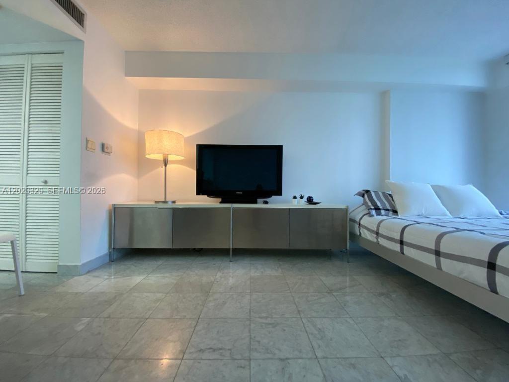 A bedroom features a television on a metal console, a floor lamp, and a bed — 540 Brickell Key Dr # 913, Miami FL 33131, MIAMI, FL