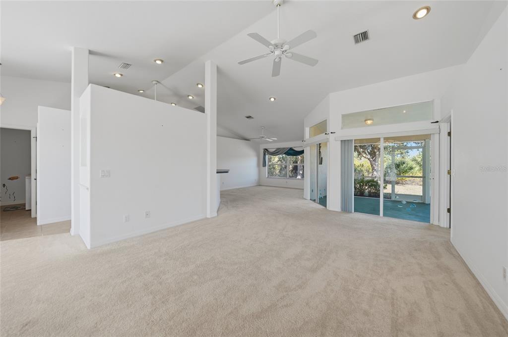 A spacious living room with beige carpeting, vaulted ceilings, a ceiling fan, and sliding glass doors — 13452 CEDAR CITY AVENUE, PORT CHARLOTTE, FL