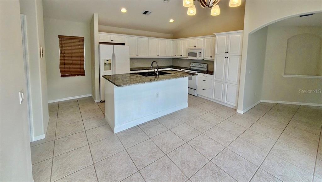 A kitchen features white cabinets, a granite-topped island, and light tile flooring — 229 VENICE PALMS BOULEVARD, VENICE, FL