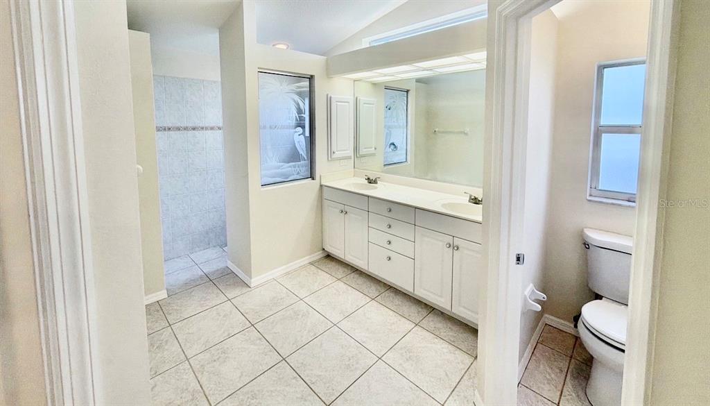 A bathroom features white cabinetry, a double vanity, a tiled floor, and a separate toilet — 229 VENICE PALMS BOULEVARD, VENICE, FL