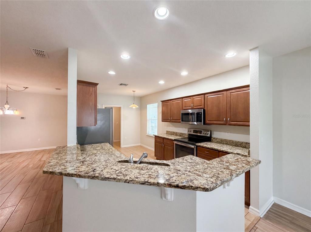 A kitchen features wood cabinets, granite countertops, a breakfast bar, and stainless steel appliances — 1048 BETHPAGE ROAD, AUBURNDALE, FL