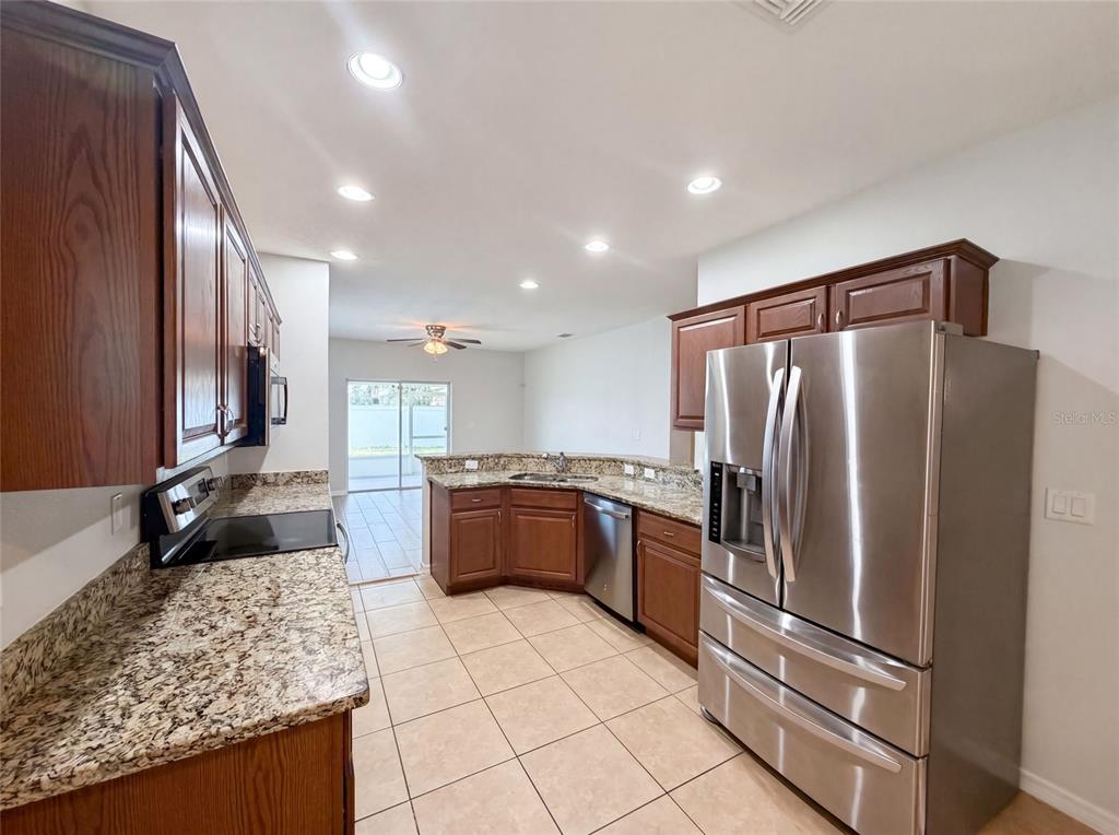 A kitchen with wood cabinets, granite countertops, stainless steel appliances, and tile flooring — 1048 BETHPAGE ROAD, AUBURNDALE, FL