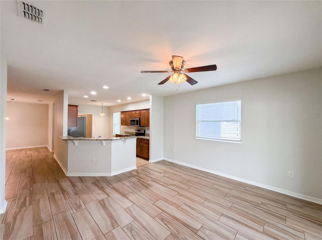 An open-concept living area features wood-look tile flooring, a ceiling fan, and a kitchen — 1048 BETHPAGE ROAD, AUBURNDALE, FL