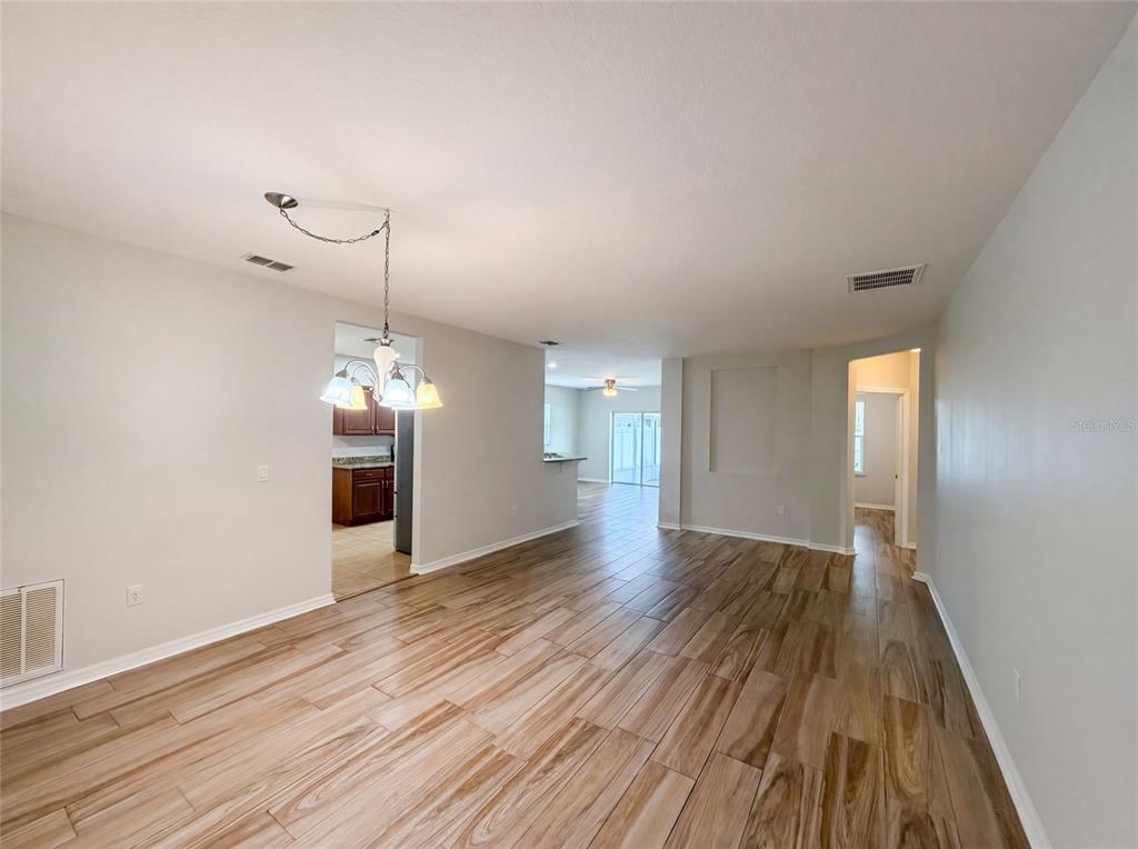 An open-concept living and dining area features light wood-look tile flooring and a chandelier — 1048 BETHPAGE ROAD, AUBURNDALE, FL