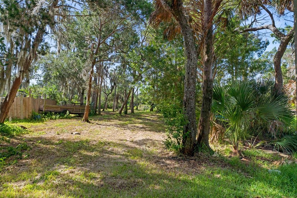 A grassy, wooded lot features a wooden fence and a utility trailer on the left — 14512 W BLACK CREEK DRIVE, CRYSTAL RIVER, FL