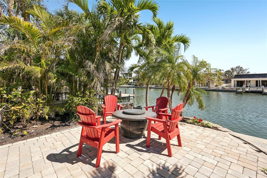Four red Adirondack chairs surround a fire pit on a paved patio by the water — 85 S POLK DRIVE, SARASOTA, FL