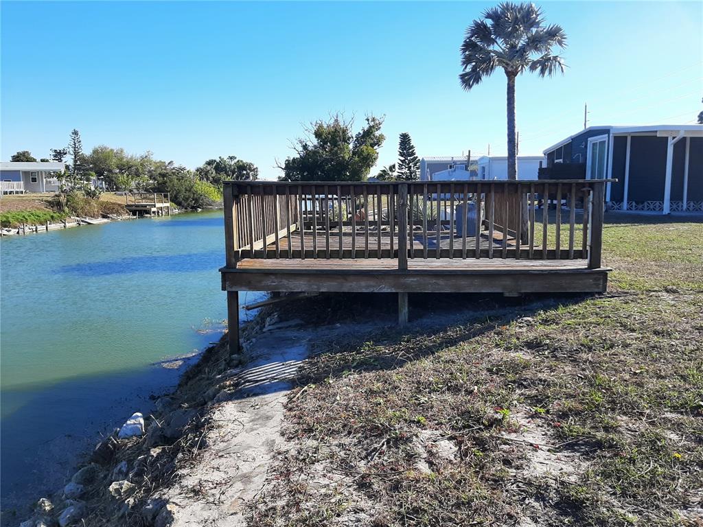 A wooden deck overlooks a canal next to a mobile home under a clear sky — 1347 FLAMINGO DRIVE, ENGLEWOOD, FL