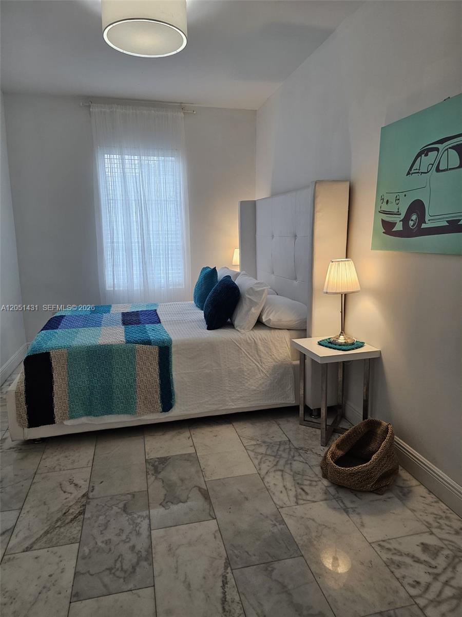A bedroom features a white tufted headboard, a blue patterned throw, and marble tile flooring — 918 Jefferson Ave # 8, Miami Beach FL 33139, MIAMI BEACH, FL