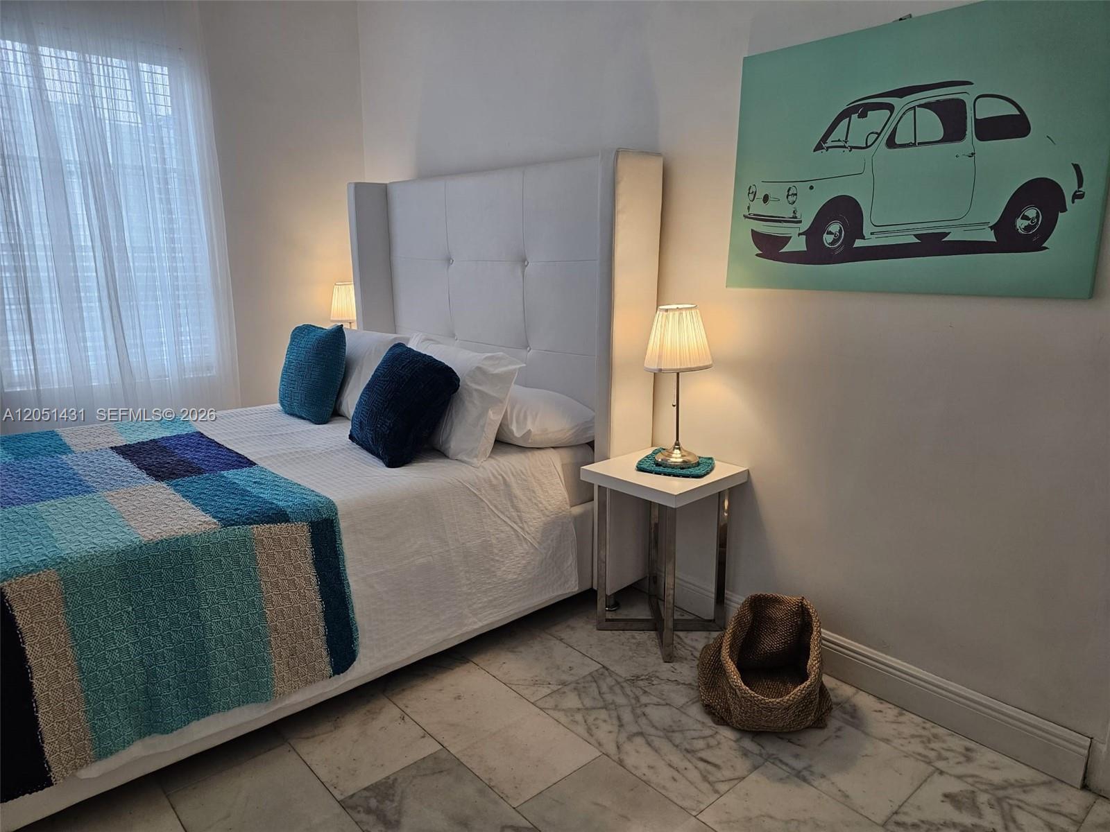 A bedroom features a white tufted headboard, marble flooring, and a teal car wall art piece — 918 Jefferson Ave # 8, Miami Beach FL 33139, MIAMI BEACH, FL