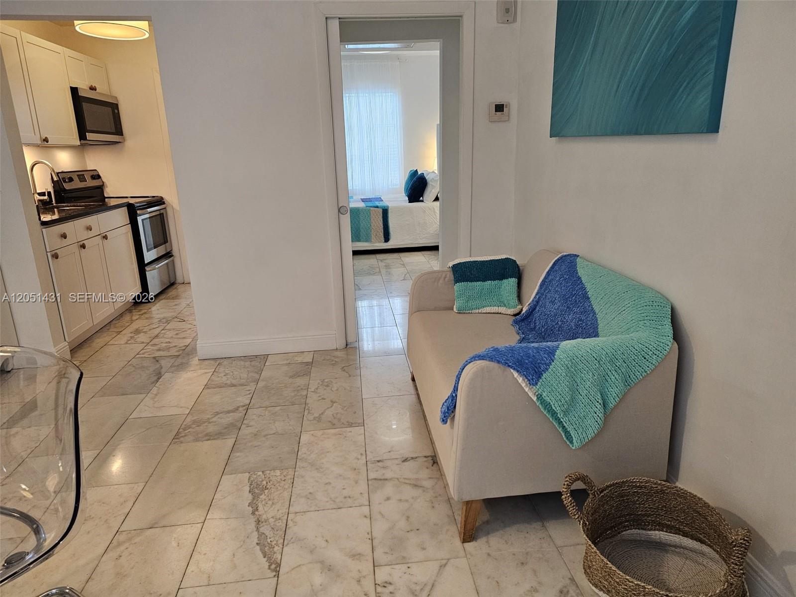 A beige loveseat sits on a marble floor near a kitchen and a bedroom doorway — 918 Jefferson Ave # 8, Miami Beach FL 33139, MIAMI BEACH, FL