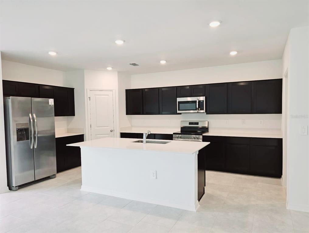 A modern kitchen features dark cabinets, white countertops, a central island, and stainless steel appliances — 1454 AUSTIN ST, WINTER HAVEN, FL