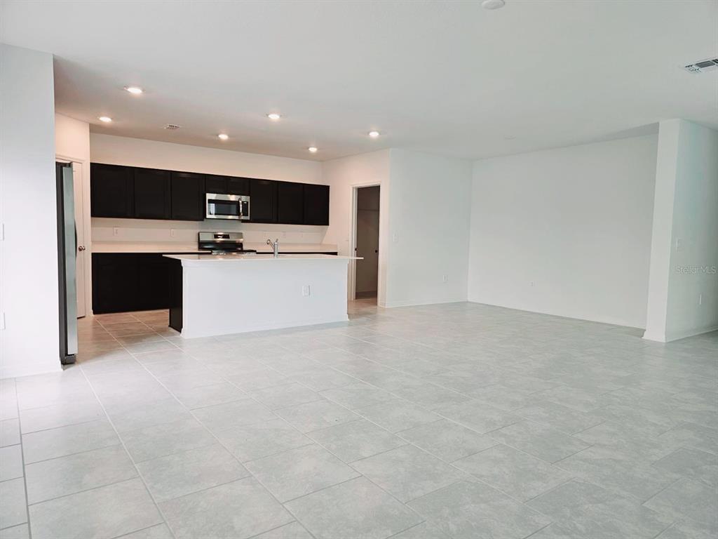 A kitchen with dark cabinets and a white island opens into a large tiled room — 1454 AUSTIN ST, WINTER HAVEN, FL