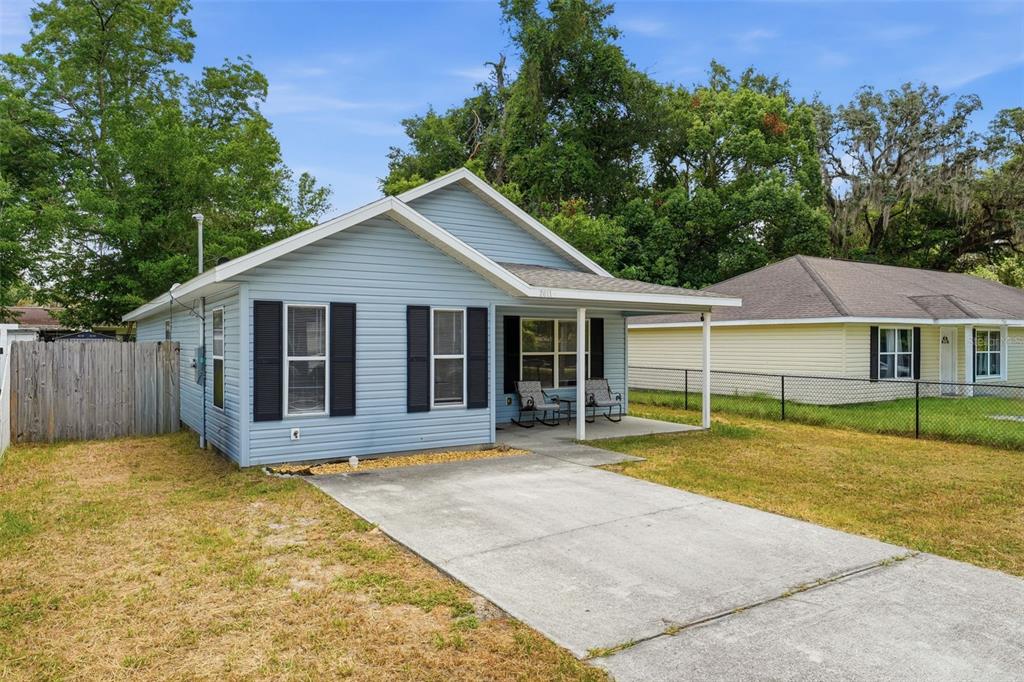 A light blue, single-story house with black shutters and a concrete driveway sits on grass — 2611 NW 1ST AVENUE, OCALA, FL