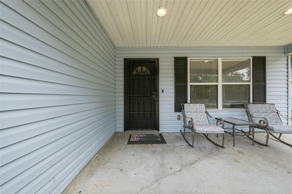 A covered front porch features light blue siding, a black security door, and two rocking chairs — 2611 NW 1ST AVENUE, OCALA, FL