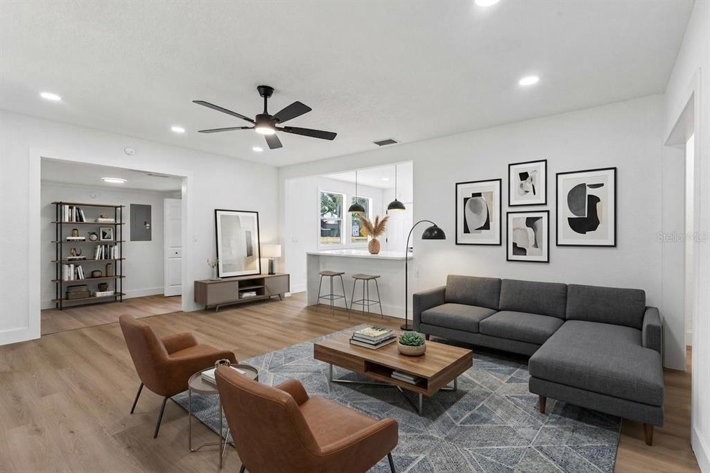 A modern living room features a grey sectional sofa, two brown chairs, and wood flooring — 1910 CURRY FORD ROAD, ORLANDO, FL