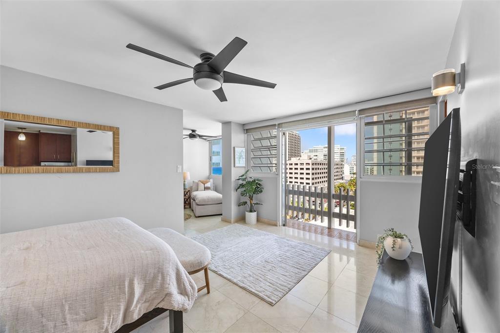 A bedroom with a ceiling fan, tiled floors, and a balcony overlooking city buildings — 1126 ASHFORD AVENUE UNIT 88, SAN JUAN, PR