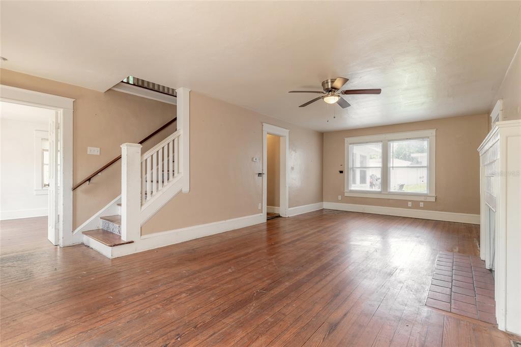 An empty living room features hardwood floors, a staircase, a ceiling fan, and a fireplace — 724 N OLEANDER AVENUE, DAYTONA BEACH, FL