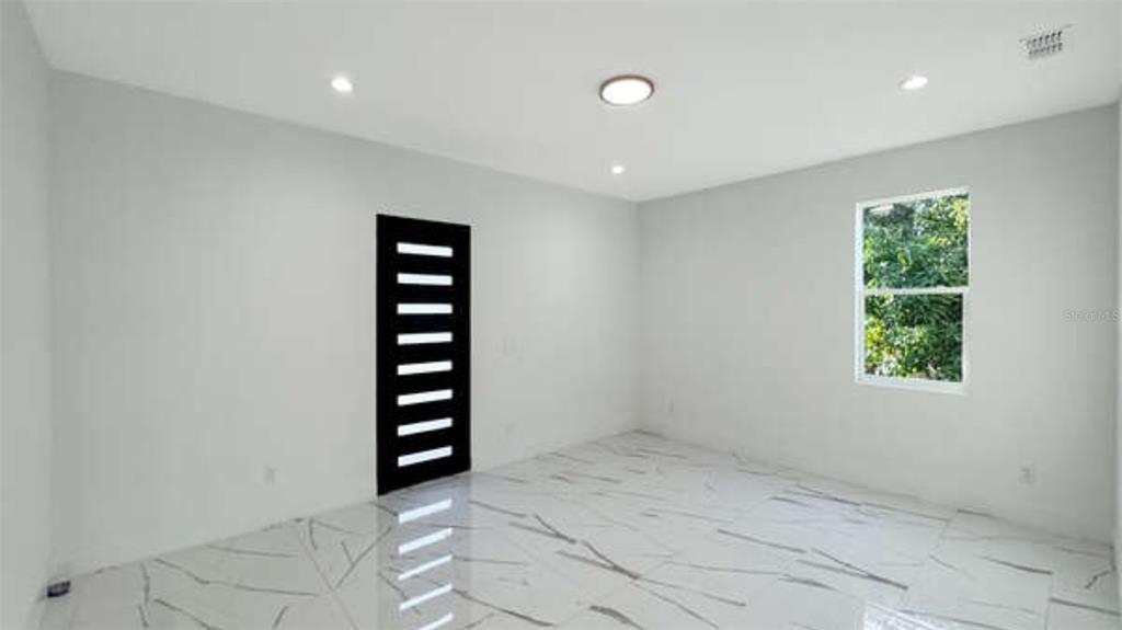 A bright, empty room features white walls, white marble-patterned tile flooring, and a modern door — 27 W 8TH STREET, APOPKA, FL