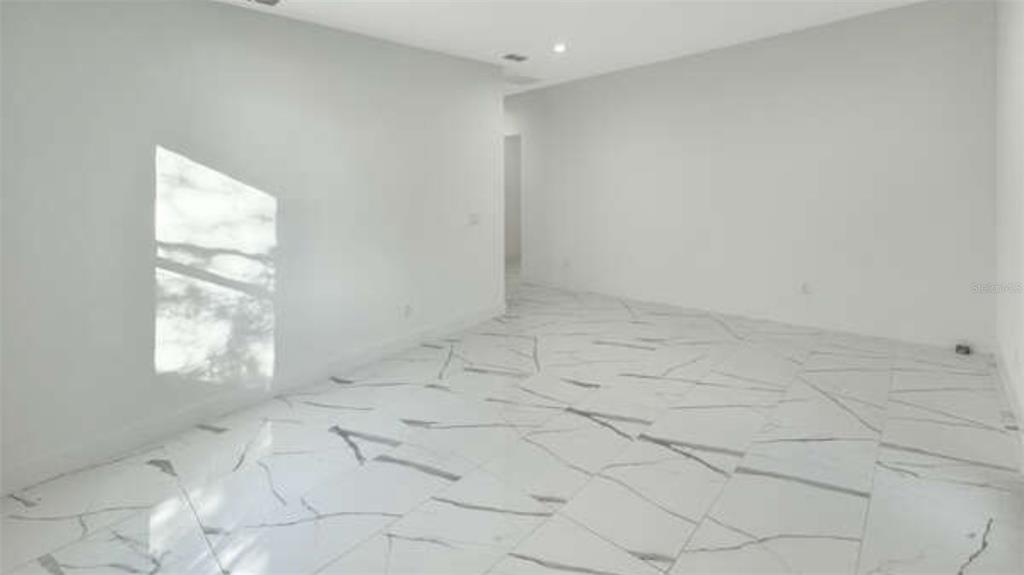 An empty room with white walls and large-format white marble-patterned tile flooring — 27 W 8TH STREET, APOPKA, FL