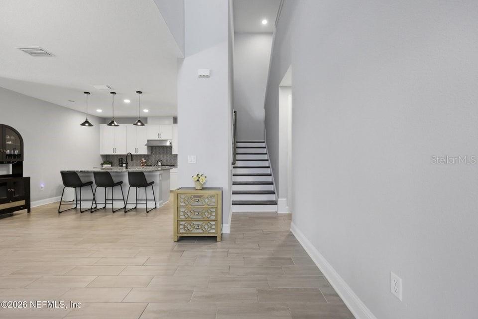 A modern kitchen with a breakfast bar and island sits beside a staircase and hallway — 10023 FILAMENT BOULEVARD, JACKSONVILLE, FL