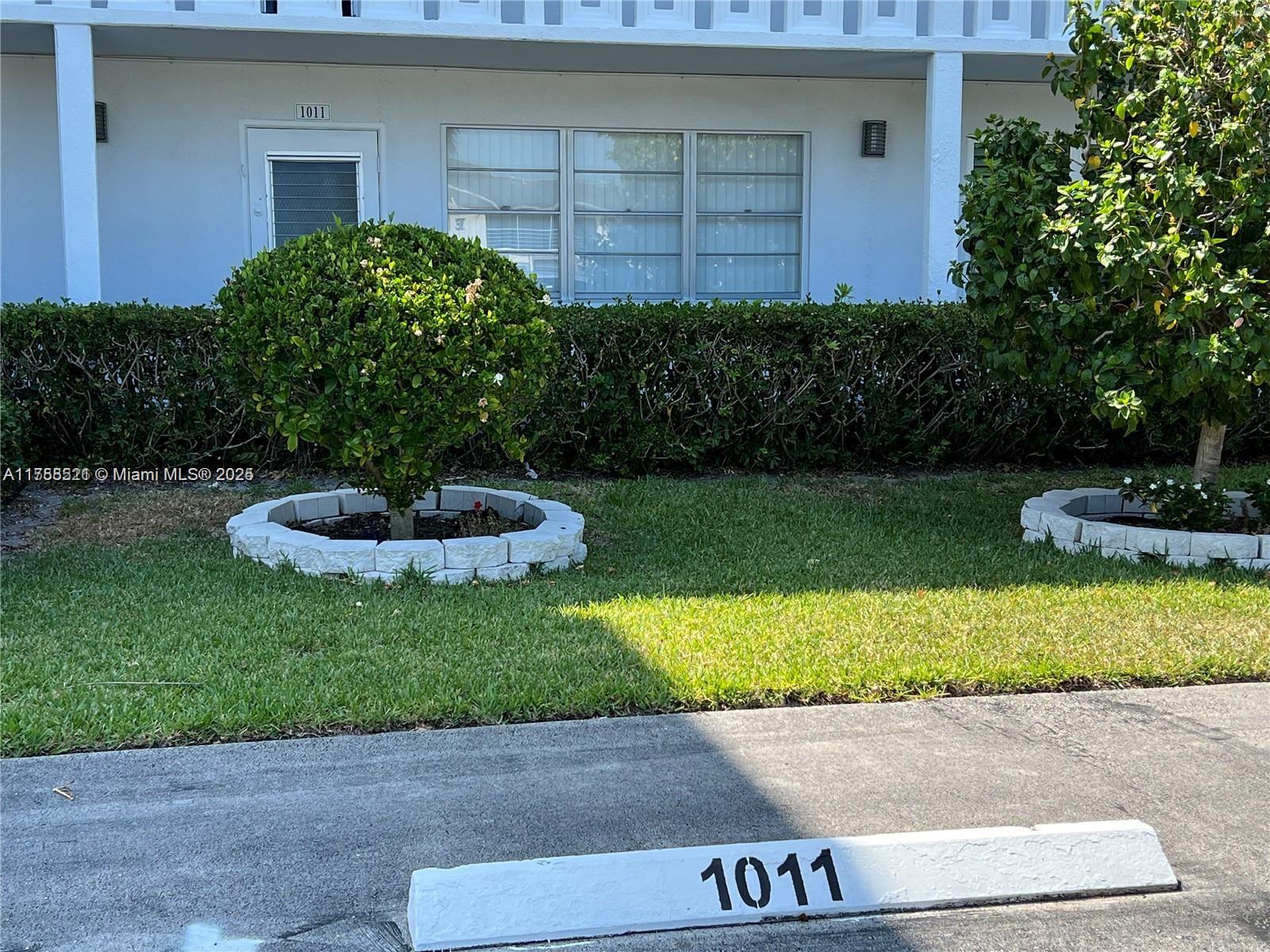 A white building exterior features a numbered door, windows, and two circular landscaped tree planters — 1011 Ellesmere A # 1011, Deerfield Beach FL 33442, DEERFIELD BEACH, FL