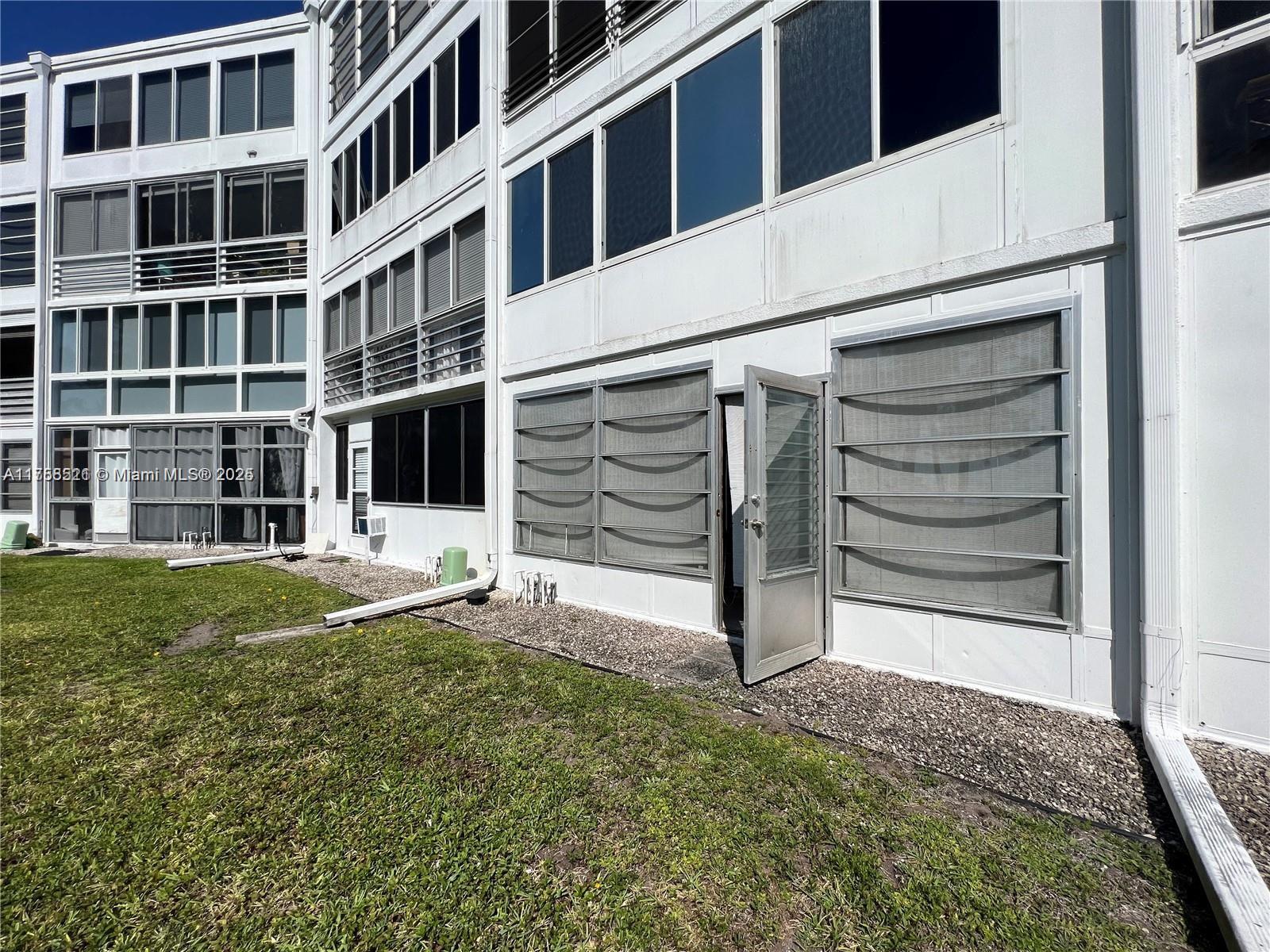 The exterior of a multi-story white building features louvered windows and a ground-level door — 1011 Ellesmere A # 1011, Deerfield Beach FL 33442, DEERFIELD BEACH, FL