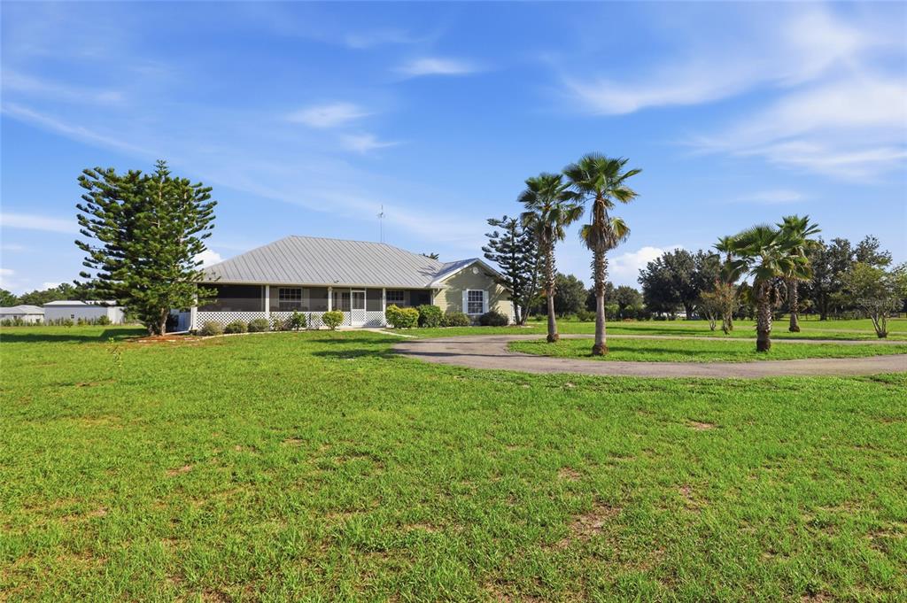 A single-story house with a metal roof and screened porch sits on a grassy lot — 1277 SW EAST CREEK TRAIL, ARCADIA, FL
