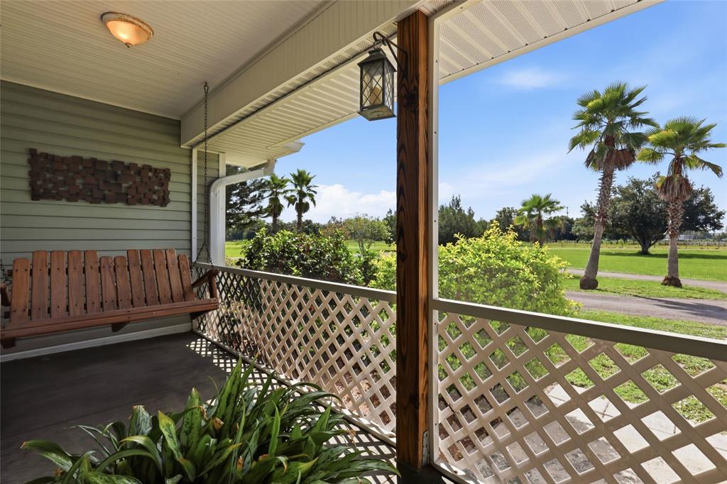 A screened-in porch features a wooden swing, lattice railings, and a view of palm trees — 1277 SW EAST CREEK TRAIL, ARCADIA, FL