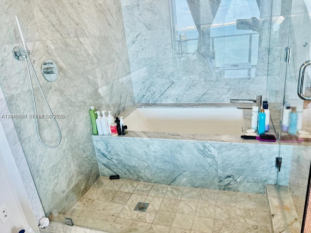 A marble-tiled bathroom features a soaking tub, a handheld shower, and a glass-enclosed shower area — 3131 NE 7th Ave # 1806, Miami FL 33137, MIAMI, FL