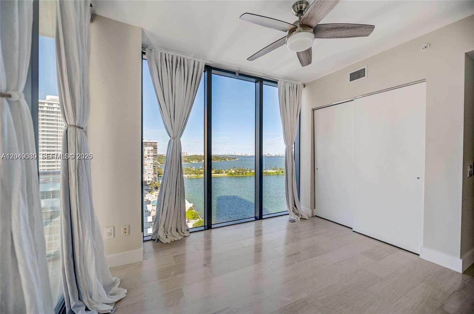 A bedroom with floor-to-ceiling windows, light wood flooring, a ceiling fan, and water views — 3131 NE 7th Ave # 1806, Miami FL 33137, MIAMI, FL