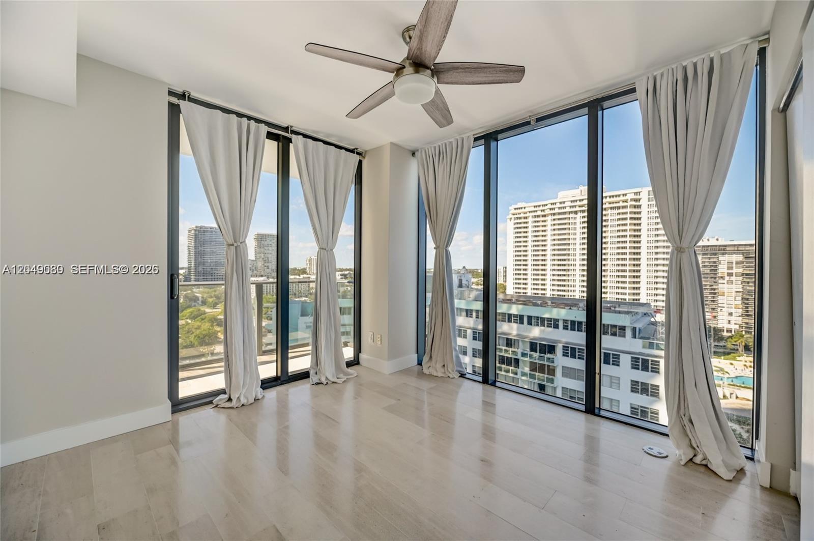 An empty room features light wood flooring, a ceiling fan, and floor-to-ceiling windows with curtains — 3131 NE 7th Ave # 1806, Miami FL 33137, MIAMI, FL