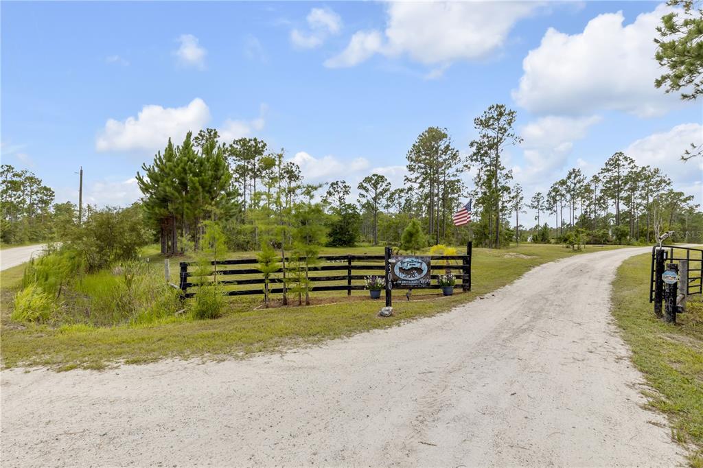 An aerial view shows a house, a detached garage, and a pond on a wooded lot — 300 OMEGA RANCH ROAD, NEW SMYRNA BEACH, FL