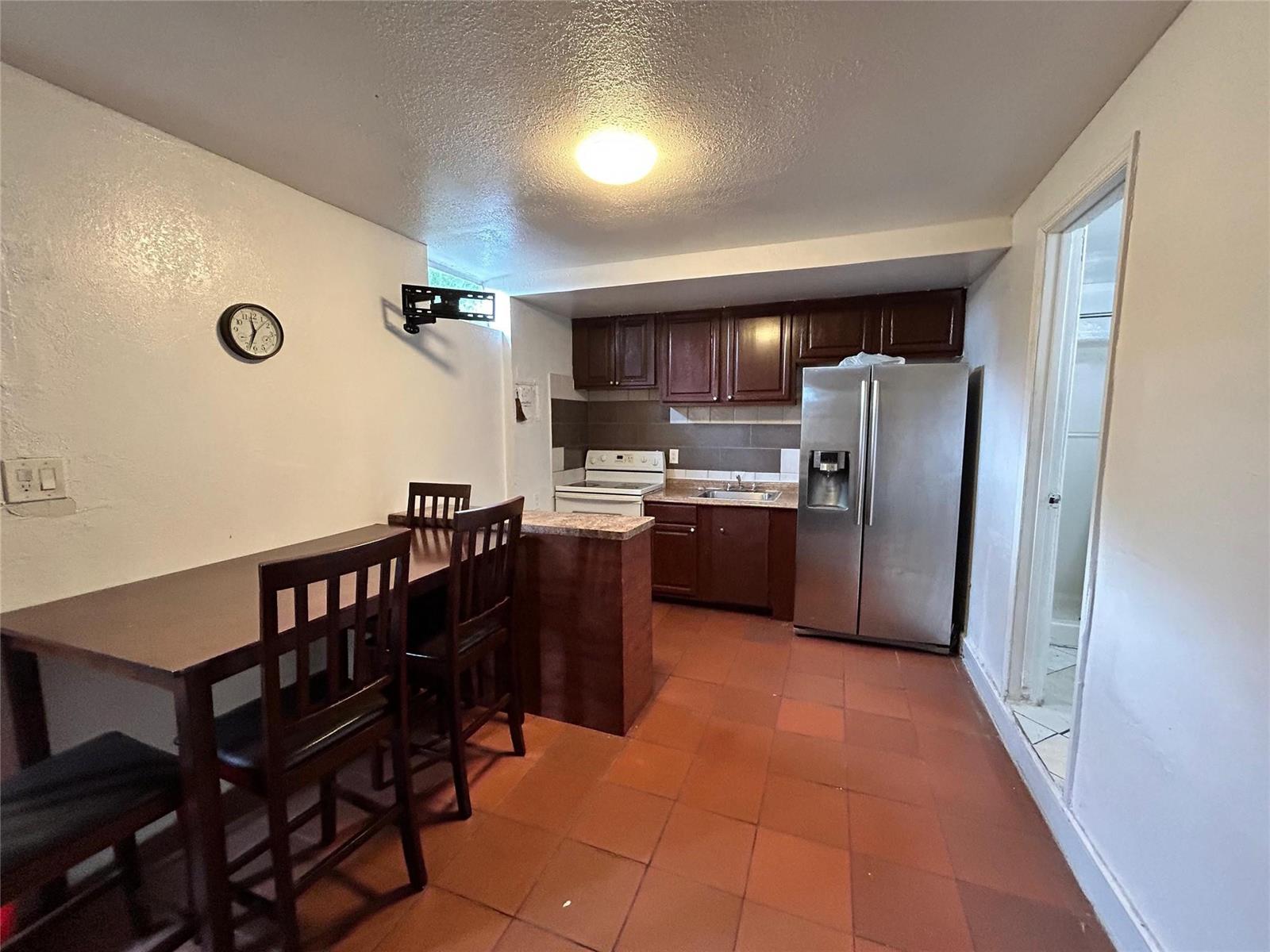 A kitchen features dark wood cabinets, stainless steel appliances, and a dining table with chairs — 112 Newton Road, West Park FL 33023, WEST PARK, FL