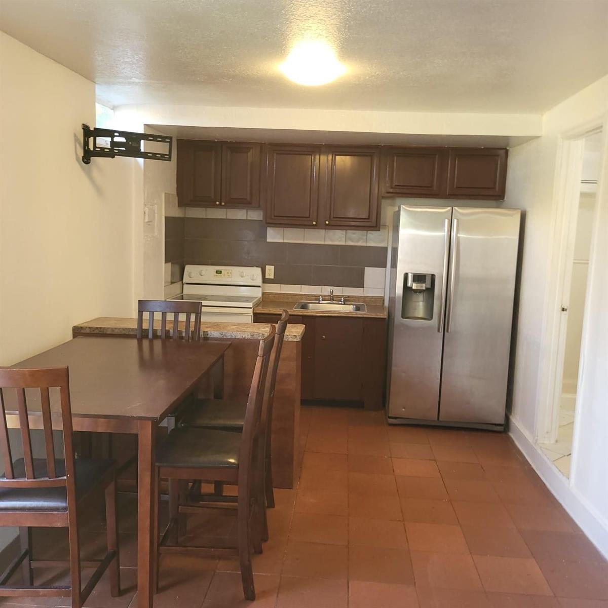 A small kitchen features dark wood cabinets, stainless steel appliances, and a dining table — 112 Newton Road, West Park FL 33023, WEST PARK, FL