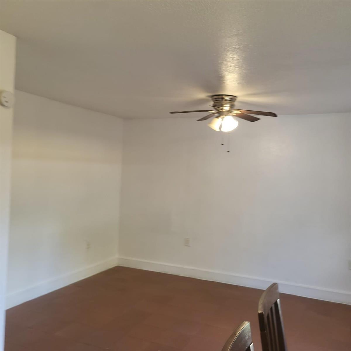 An empty room with white walls, brown flooring, and a ceiling fan with light fixtures — 112 Newton Road, West Park FL 33023, WEST PARK, FL