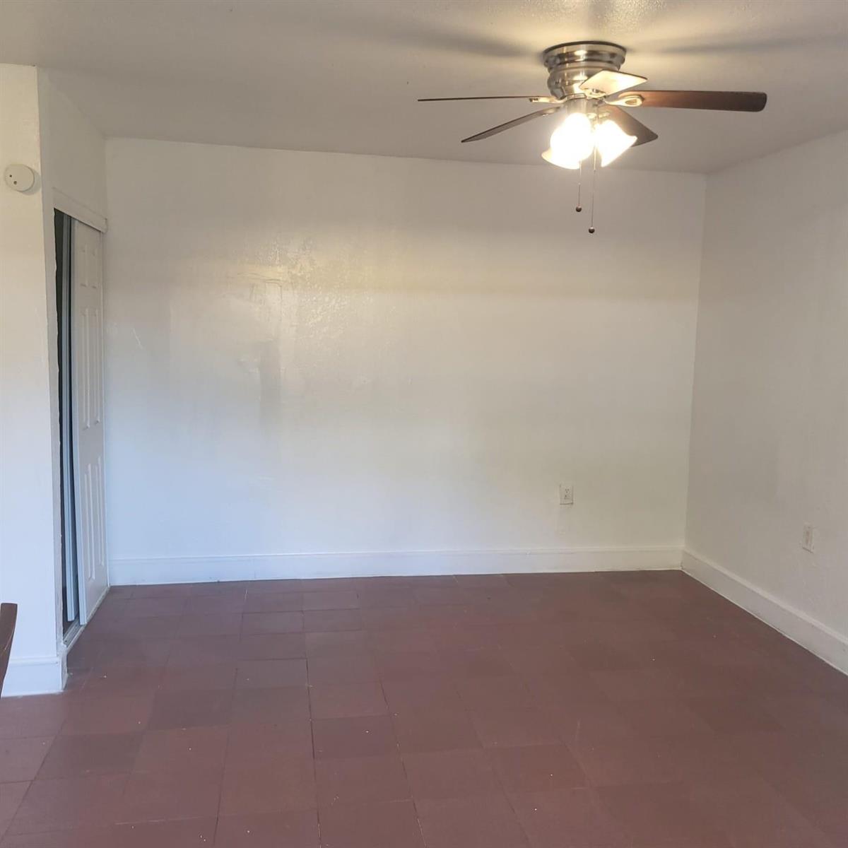 An empty room with white walls, a ceiling fan, and brown square floor tiles — 112 Newton Road, West Park FL 33023, WEST PARK, FL