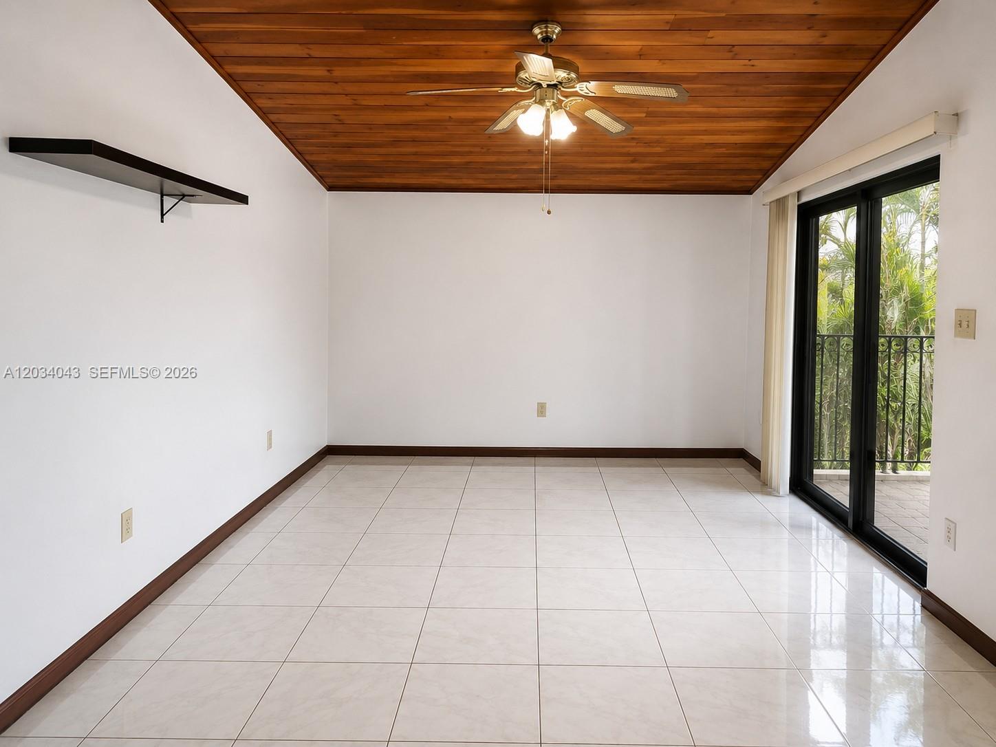 An empty room features white walls, tiled floors, a wood-paneled ceiling, and sliding glass doors — 6521 SW 114th Ave, Miami FL 33173, MIAMI, FL