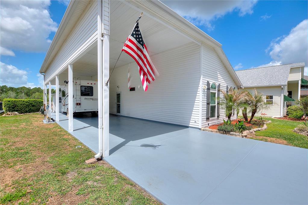 A white house features a large covered carport with a painted floor and American flag — 1083 MOTORCOACH DRIVE, POLK CITY, FL