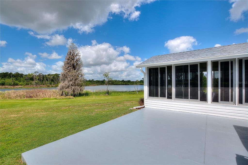 A gray concrete patio sits beside a white house with a screened-in porch overlooking a lake — 1083 MOTORCOACH DRIVE, POLK CITY, FL