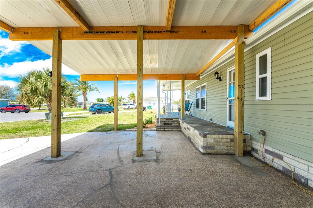 A covered concrete patio features wooden support beams and a stone-faced porch entry — 6115 SHEARWATER DRIVE, ENGLEWOOD, FL