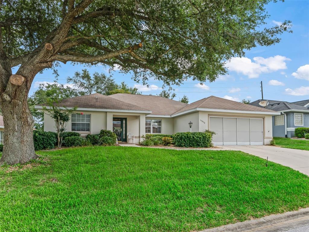 A single-story house with a tan exterior, a two-car garage, and a large shade tree — 17076 SE 115TH TERRACE ROAD, SUMMERFIELD, FL