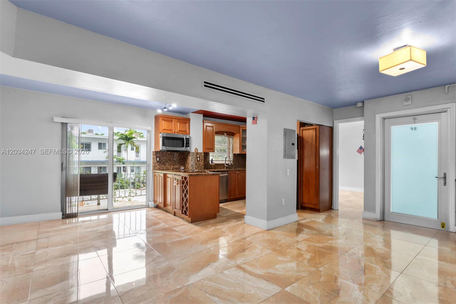 A kitchen with wood cabinets and granite countertops opens to a living area with tile — 1820 James Ave # 2F, Miami Beach FL 33139, MIAMI BEACH, FL