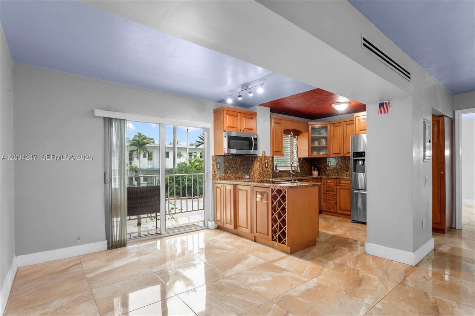 This kitchen features wood cabinets, granite countertops, and a sliding glass door to a balcony — 1820 James Ave # 2F, Miami Beach FL 33139, MIAMI BEACH, FL